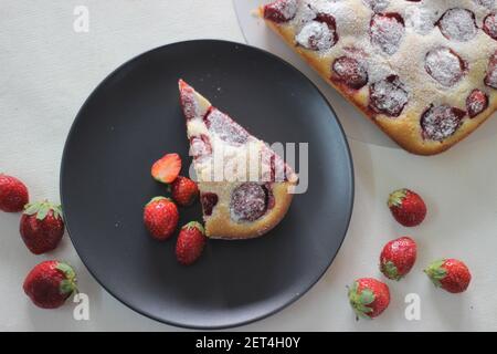Hausgemachter Erdbeerkuchen. Ein einfacher gelber Kuchen mit vielen frischen Erdbeeren und Puderzucker darauf bestreut. Aufnahme auf weißem Hintergrund Stockfoto