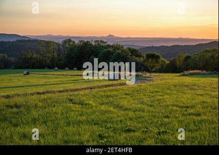 Ländliche Landschaft des tschechischen Paradies in Sonnenuntergang Beleuchtung. Wiese, Wald und Silhouette der Hügel mit Burg Bezdez am Horizont. Mirova pod Kozakovem, CZ. Stockfoto