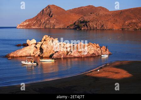 Meeresküste, Sandstrand und Riff mit Booten in kleinem Hafen in schöner warmer Beleuchtung bei Sonnenaufgang. Lemnos Insel, Agios Ioannis, Griechenland. Stockfoto