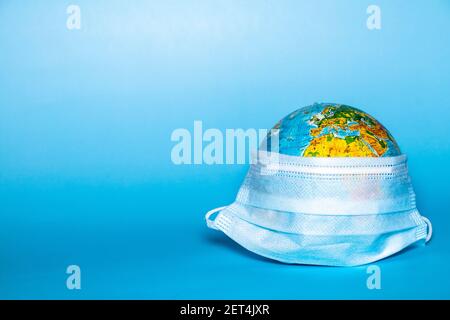 Weltweite Pandemie. COVID-19 Virenkonzept mit Globus in chirurgischer Gesichtsmaske auf blauem Hintergrund mit Platz für Text und Kopierraum. Stockfoto