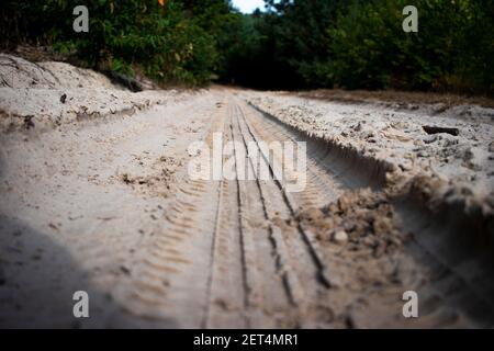 Radprofildruck auf einer sandigen Straße im Wald. Bedecke die Spuren schmutziger Reifen auf dem Boden. Offroad-Hintergrund. Stockfoto