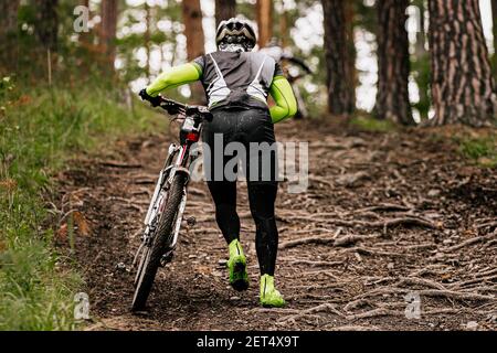 Rückfahrer mit Mountainbike geht bergauf auf auf Trail mit Baumwurzeln Stockfoto