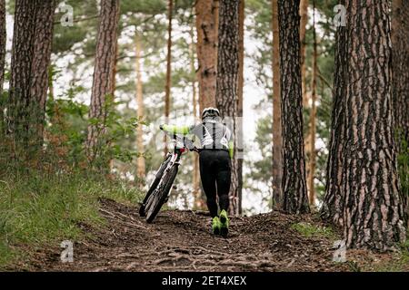 Mann Radfahrer mit Mountainbike geht bergauf auf Trail mit Baumwurzeln Stockfoto