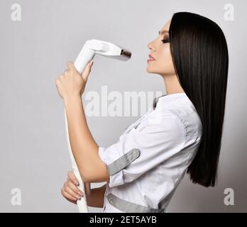 Profil von jungen hübschen Brünette Frau in weißer Kleidung stehen Und Haltevorrichtungen für die Laser-Haarentfernung Stockfoto