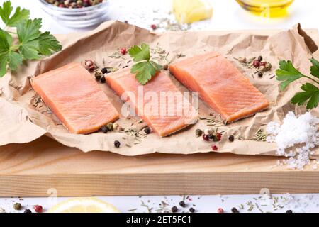Drei Filets von frischem rohem Lachsfisch mit Gewürzen und Kräutern auf Schneidebrett. Stockfoto