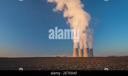 Temelin, Tschechische republik - 02 28 2021: Kernkraftwerk Temelin, dampfende Kühltürme in der Landschaft bei Sonnenuntergang, Feld im Vordergrund Stockfoto