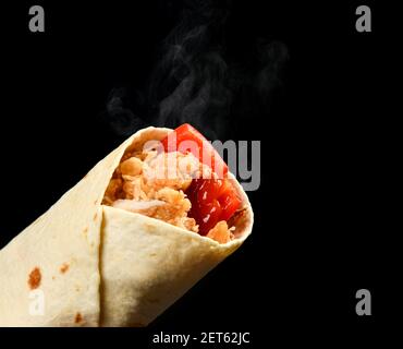 Klassische Tortilla-Wrap-Rolle mit gegrilltem knusprigem Huhn oder pute und Gemüse, Tomaten, Paprikapfeffer mit Dampfrauch auf Schwarz Stockfoto