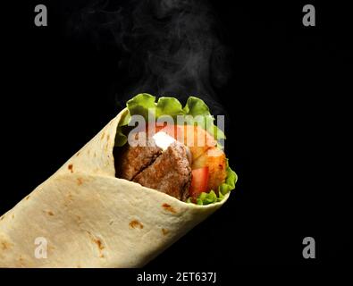 Klassische Tortilla Wrap Roll mit gegrilltem Rindfleisch, Käse und Gemüse, Tomaten, Salat mit Dampfrauch auf schwarz Stockfoto