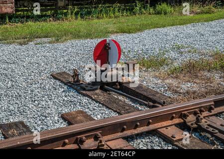 Ein runder rot-weißer Bahnsignalschalter neben dem Gleise verschraubt auf Bindungen in Schotter in einem gesetzt Güterbahnhof an einem sonnigen Tag im Sommer Stockfoto