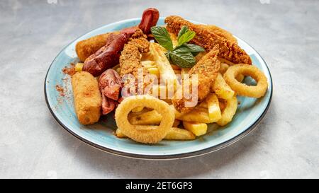 Pommes Frites, Zwiebelringe und Hähnchenflügel auf blauem Teller auf blaugrauem Hintergrund Stockfoto