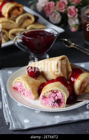 Hausgemachte Pfannkuchen mit Quark Füllung und Kirsche, serviert mit Kirschsauce auf einem Teller auf dunklem Hintergrund. Vertikales Format Stockfoto