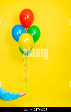 Weibliche Hand halten ein Bündel von bunten Ballons. Party oder Present Konzept. Grüne, rote, gelbe und blaue Luftballons und Hand isoliert auf gelbem Hintergrund. Stockfoto