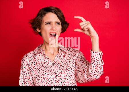 Portrait von schönen enttäuscht unzufrieden braune haarige Mädchen zeigt winzige Größe Isoliert über hellrotem Hintergrund Stockfoto