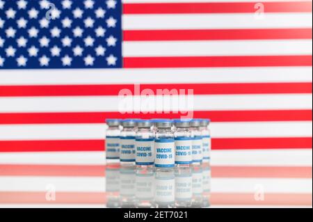 Gruppe von Vials mit einem neuen Coronavirus-Impfstoff mit einer amerikanischen Flagge im Hintergrund. Schutz vor Virusverbreitung Stockfoto