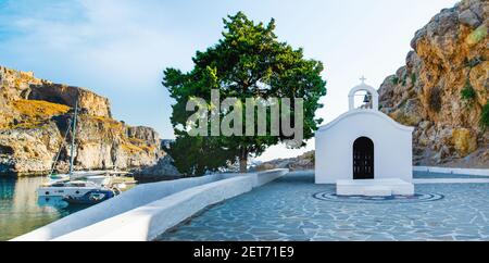 Sonnenuntergang Panorama-Landschaft der schönen St. Paul's Bay auf Rhodos Insel mit kleiner Kapelle, felsigen Strand und Jachthafen Stockfoto