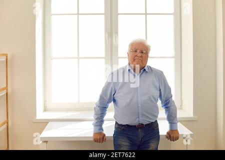 Porträt eines ernsthaften älteren Mannes, der im Stehen auf die Kamera schaut In der Nähe des Fensters Stockfoto