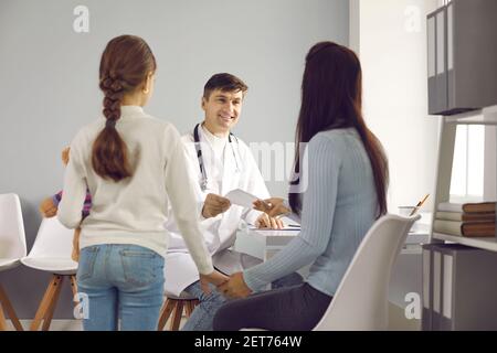 Der Arzt gibt der Mutter eines kleinen Mädchens nach ihrer ärztlichen Untersuchung ein Rezept für Medikamente. Stockfoto