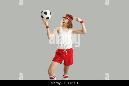 Lustige verrückte nerdy Mann in Brille, Stirnband, Tank Top und Shorts halten einen Fußball Stockfoto