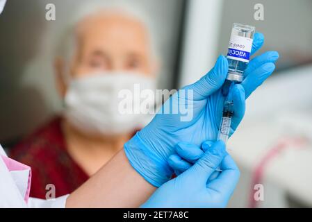 Eine Krankenschwester hält eine Spritze und ein beschriftetes Glasgefäß Covid-19 Impfstoff und bereitet sich auf die Impfung einer älteren Frau vor Stockfoto