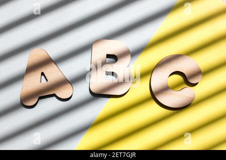 Holzbuchstaben ABC auf blauem und gelbem Hintergrund. Das Konzept der Bedeutung von Bildung. Hintergrund mit diagonalen Schatten. Stockfoto