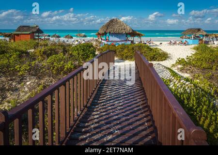 Cayo Santa Maria, Kuba, Februar 2016 - Strandpromenade zum exotischen Strand mit Urlaubern Sonnenbaden rund um Stroh geschlüpften Unterstände Stockfoto