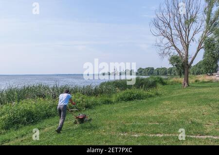 Rostow Weliki, Russland-29. Juli 2020. Ein professioneller Gärtner schneidet Gras mit elektrischer Ausrüstung in einem Outdoor-Park am Lake Nero. Stockfoto