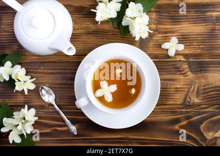 Jasmin grüner Tee in der weißen Tasse, Teekanne und Blumen auf dem braunen Holzhintergrund. Draufsicht. Speicherplatz kopieren. Stockfoto