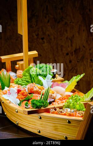 Sushi Sashimi in einem Holzboot auf einem braunen Holztisch. Mit Melodie, Garnelen, Garnelen, Ingwer Stockfoto