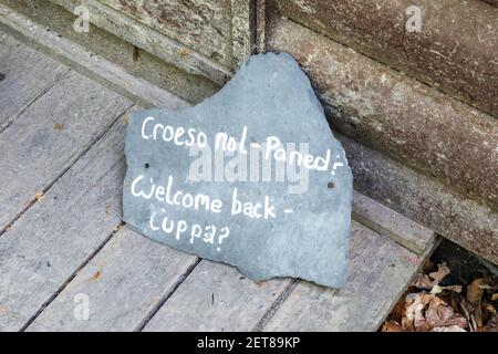 Ein Schieferschild in Walisisch und Englisch: 'Welcome back - cuppa?' Im RSPB Nature Reserve in Ynys-hir, Wales, Großbritannien Stockfoto