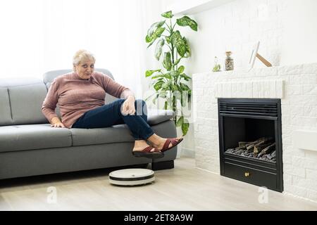 Eine ältere Frau verwendet einen Roboter-Staubsauger in einem Wohnung Stockfoto