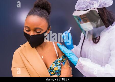 Eine afroamerikanische junge Frau, die die Injektion des COVID-19 erhält Impfstoff durch einen Arzt Stockfoto