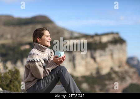 Glücklicher Wanderer, der Kaffee trinkt und dabei die Aussicht betrachtet, in der er sitzt Der Berg im Winter Stockfoto