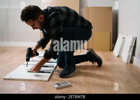 Mann hockte auf dem Boden und monierte ein Möbelstück. Machen Sie es selbst Möbelmontage. Stockfoto