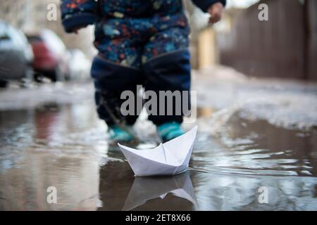 Kleiner Junge spielt mit Papier Schiffe in einer Pfütze Frühling Stockfoto