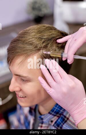 Männliche Klient erhalten Injektionen in den Kopf. Bekämpfung von Haarausfall bei Männern. Unkenntlich weibliche Kosmetikerin Hände Trichologe und den Kopf Nahaufnahme. Fokus Stockfoto