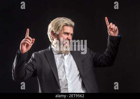 Fröhlicher, junger Geschäftsmann in schwarzem Anzug, der Musik mit Kopfhörern hört und auf grauem Hintergrund tanzt. Stockfoto