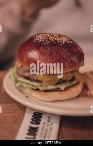 Ein vertikaler Schuss eines leckeren Hamburgers auf dem weißen Platte auf dem unscharfen Hintergrund Stockfoto