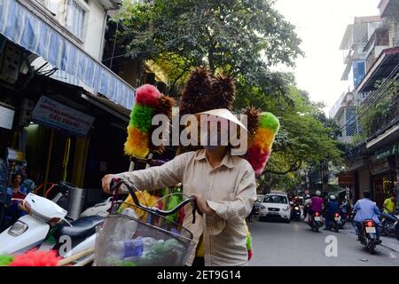 Hanoi, Vietnam - September, 2015: Vietnamesische Frau in Maske zu Fuß mit dem Fahrrad und Verkauf bunte Federduster auf der Straße der Stadt Stockfoto