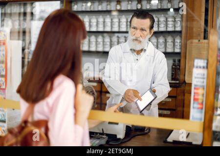 Medizin, Pharmazie und Menschen Konzept. Schöner bärtiger kaukasischer Mann Apotheker, zeigt auf e-Rezept auf Tablet-pc, coversulting Stockfoto