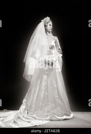 1940S JUNGE FRAU BRAUT IM HOCHZEITSKLEID LANGE ÄRMEL AUSSCHNITT SPITZE ZUG TIARA UND SCHLEIER VOLLER LÄNGE POSE STEHEN IN PROFILE - B4601 HAR001 HARS STUDIO SHOT HEALTHINESS COPY SPACE IN VOLLER LÄNGE DAMEN PERSONEN SATIN SCHLEIER GELASSENHEIT TIARA SPIRITUALITÄT VERTRAUEN B & W BRIDAL DREAMS GLÜCK WELLNESS BRÄUTE UND AUFREGUNG STOLZ IN GEHOBENE KONZEPTIONELLE WOHLHABENDE ÄRMEL STILVOLLE POSE GUT ZU TUN JUNGE ERWACHSENE FRAU SCHWARZ UND WEISS KAUKASISCHEN ETHNIZITÄT HAR001 AUSSCHNITT ALTMODISCH Stockfoto