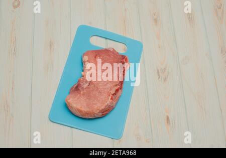 Rohe Schweinesteaks liegen auf einem blauen Brett. Appetitliches Fleisch. Schweinefleisch auf blauem Brett auf blauem Hintergrund Stockfoto