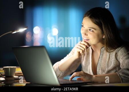 Nachdenklicher Unternehmer, der mit einem Laptop arbeitet und sich fragt, ob er seitwärts schaut Die Nacht zu Hause Stockfoto