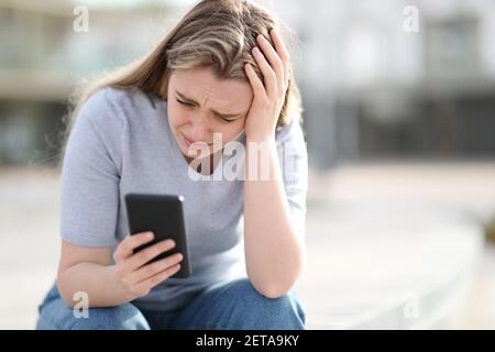 Trauriger Teenager, der schlechte Nachrichten auf dem Handy überprüft, beschwert sich allein Auf der Straße Stockfoto