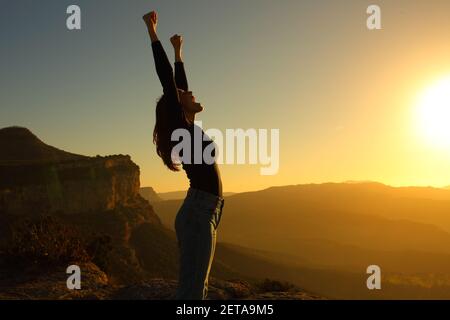 Profil einer Silhouette einer Frau, die die Arme hebt Wir feiern Urlaub bei Sonnenuntergang in den Bergen Stockfoto