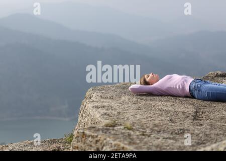 Entspannte Frau, die allein auf der Oberseite eines liegt Klippe in den Bergen Stockfoto