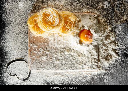 Frisch gekochte Pasta liegt auf einer dunklen, mit Mehl bestäubten Oberfläche. Italienische Pasta. Tagliatelle. Rohe Pasta. Italienische Pasta Rezept. Draufsicht, Kopierbereich. Stockfoto