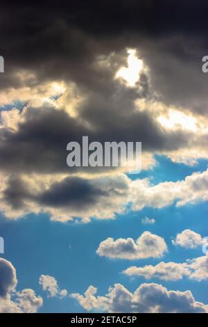 Die Sonne bricht von hinten durch lockige dunkle Wolken gegen einen blauen Himmel vor einem Sturm oder Regen im Sommer des Frühlings. Die Textur und der Hintergrund von Stockfoto