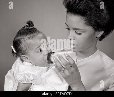 1960S AFRIKANISCH-AMERIKANISCHE FRAU MUTTER FÜTTERUNG BABY MIT FLASCHE BABYS FRAUEN MÜTTER FAMILIE FAMILIEN ELTERNSCHAFT - N2089 HAR001 HARS KOMMUNIKATIONSFLASCHEN JUNGE ERWACHSENE KLEINKIND STARKE FAMILIEN FREUDE LIFESTYLE FRAUEN VERHEIRATET STUDIO SCHUSS GESUNDHEIT ZU HAUSE LEBEN KOPIEREN RAUM FREUNDSCHAFT DAMEN TÖCHTER PERSONEN FÜRSORGLICHE FÜTTERUNG B&W MÜTTERLICHE KOPF UND SCHULTERN AFROAMERIKANISCHE VERBINDUNGSUNTERSTÜTZUNG PERSÖNLICHE BINDUNG ZUNEIGUNG ZUSAMMENARBEIT EMOTION WACHSTUM JUGENDLICHE MÜTTER ZWEISAMKEIT FRAUEN JUNGE ERWACHSENE FRAU BABY MÄDCHEN SCHWARZ UND WEISS HAR001 ALT MODISCH Stockfoto