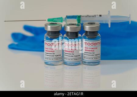 LONDON, ENGLAND - 28. FEBRUAR 2021: Drei Glasfläschchen mit Dosen des Moderna COVID Coronavirus-Impfstoffs mit einer gezogenen Spritzenspritze und Bl Stockfoto