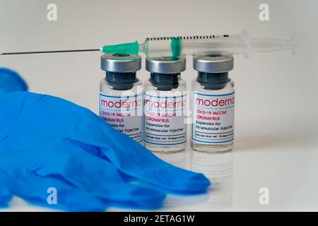 LONDON, ENGLAND - 28. FEBRUAR 2021: Drei Glasfläschchen mit Dosen des Moderna COVID Coronavirus-Impfstoffs mit einer gezogenen Spritzenspritze und Bl Stockfoto